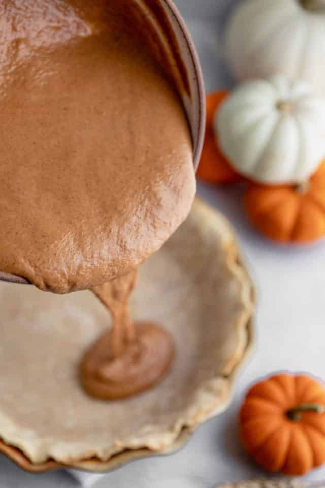 pouring pumpkin filling into a pie crust