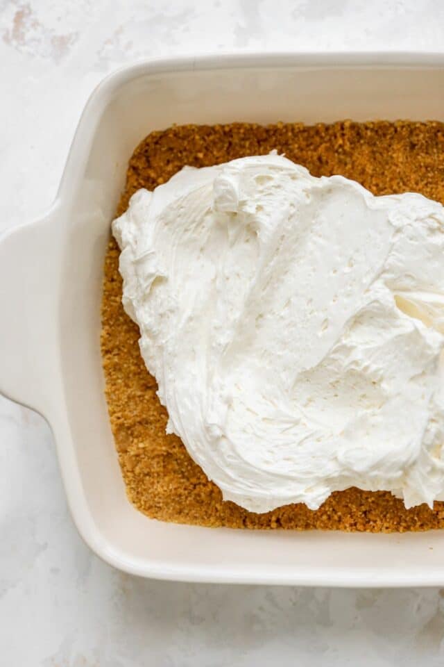 Spreading cream cheese filling over a graham cracker crust.