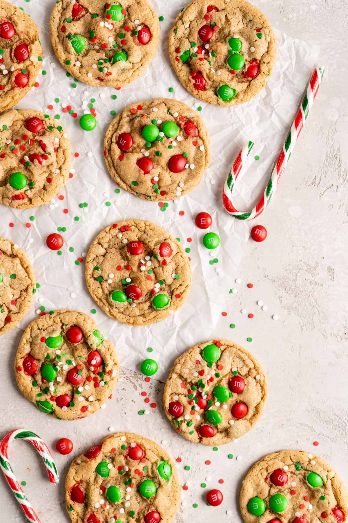 Christmas cookies with M&Ms and sprinkles on parchment paper near a candy cane.