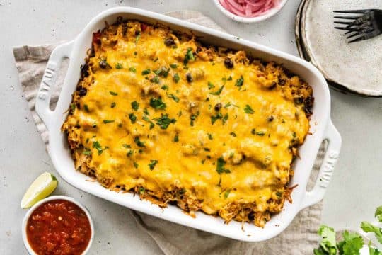 slow cooker Mexican chicken topped with cheese and baked in a white dish