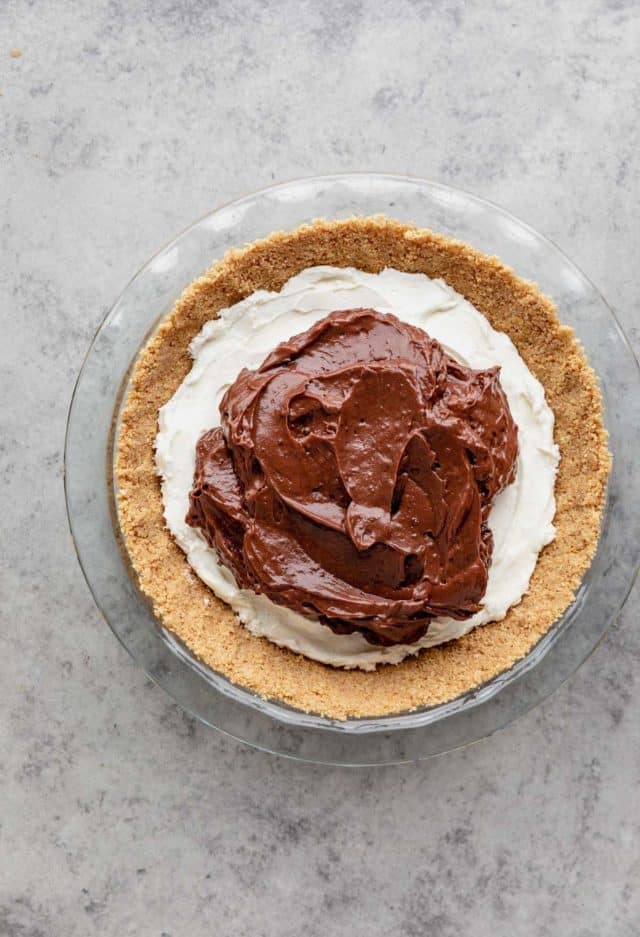 spreading chocolate pudding layer over cream cheese layer in pie crust