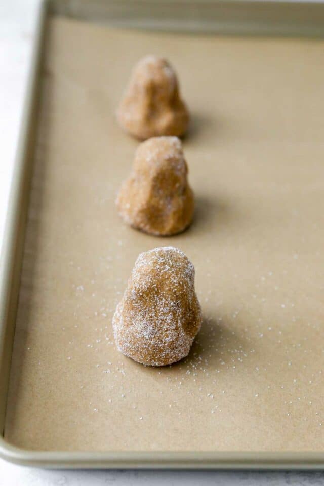 Top-heavy balls of cookie  on a lined baking sheet.