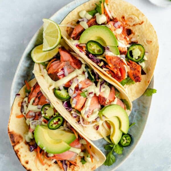 Three salmon tacos with slaw and avocado slices on a plate.