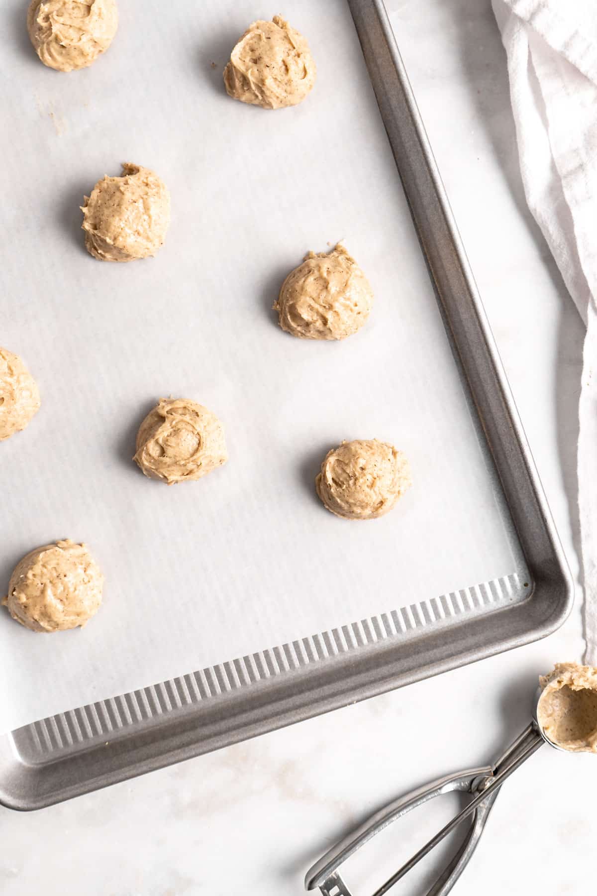 Spoonfuls of cookie batter on a parchment lined cookie sheet.