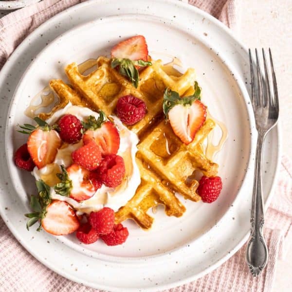 Belgian waffles served with whipped cream and fruit on a white plate