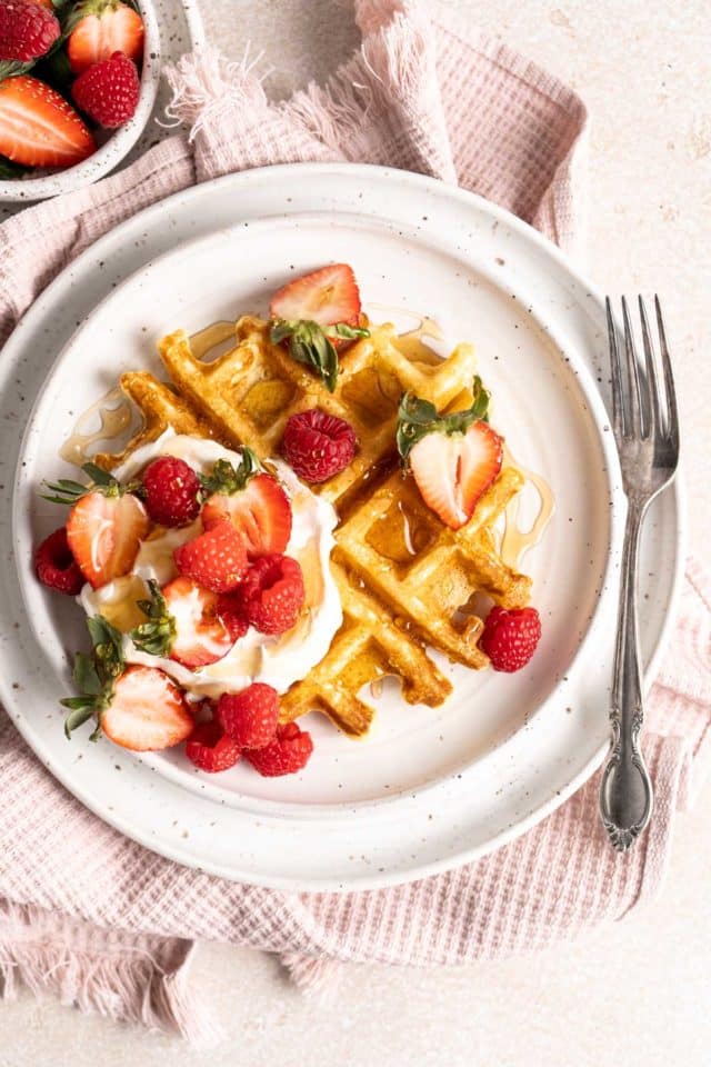 Belgian waffles served with whipped cream and fruit on a white plate