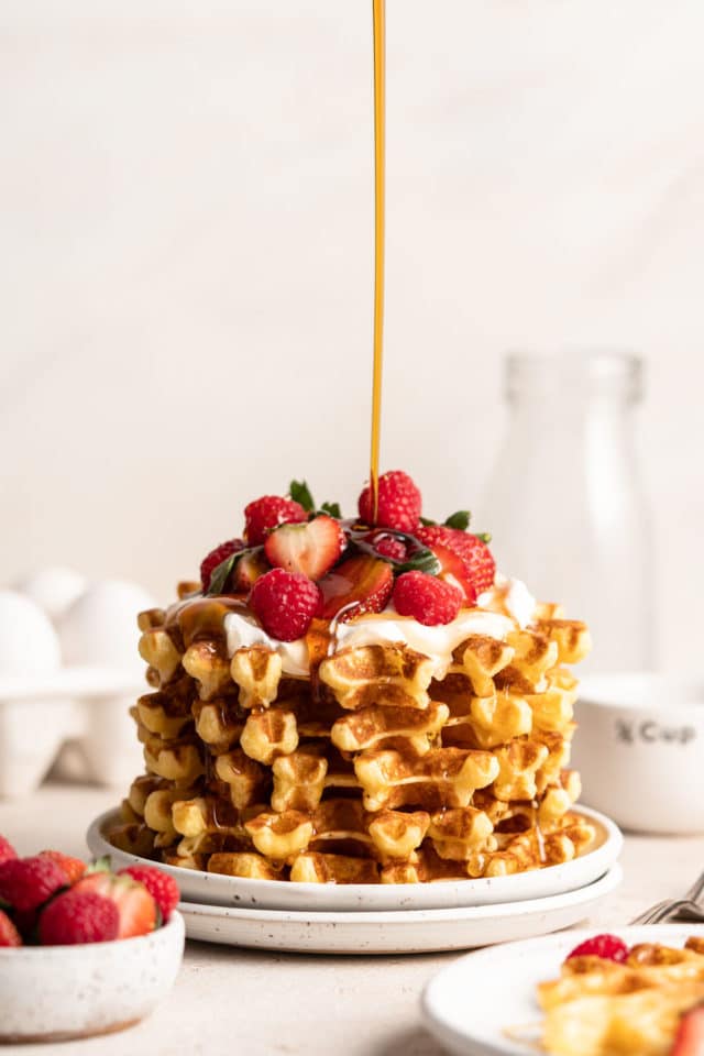 stack of Belgian waffles being drizzled with maple syrup