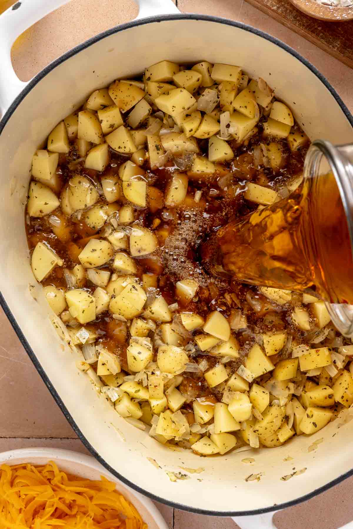 Pouring beef broth into pot with cubed potatoes.