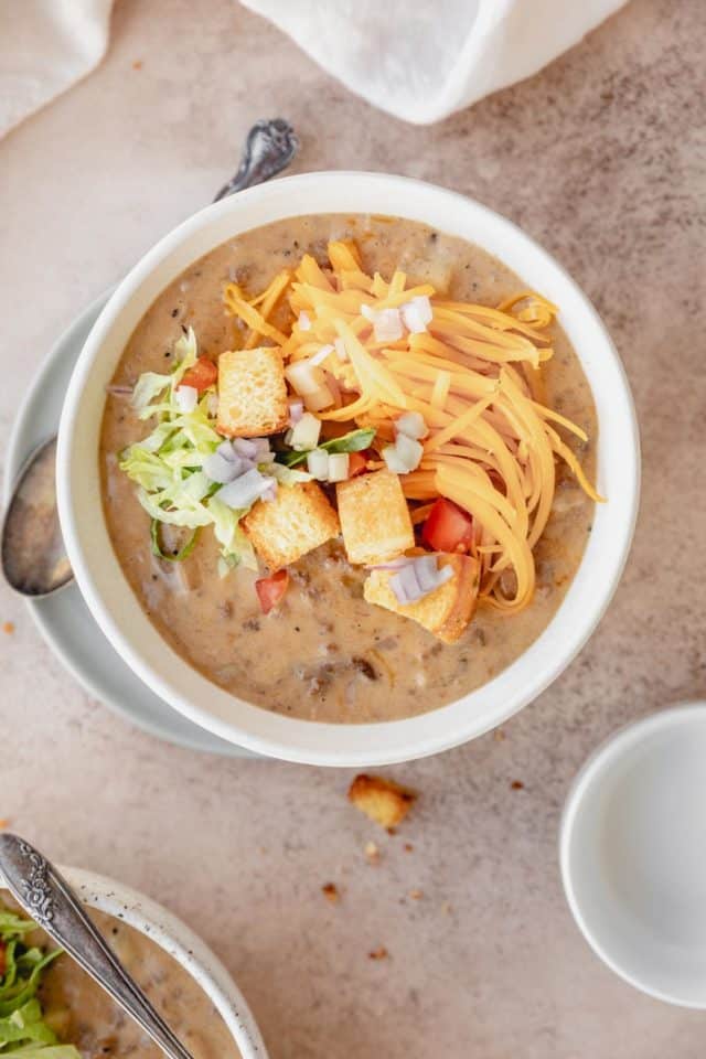 bowl of cheeseburger soup topped with croutons, cheese and other burger toppings 