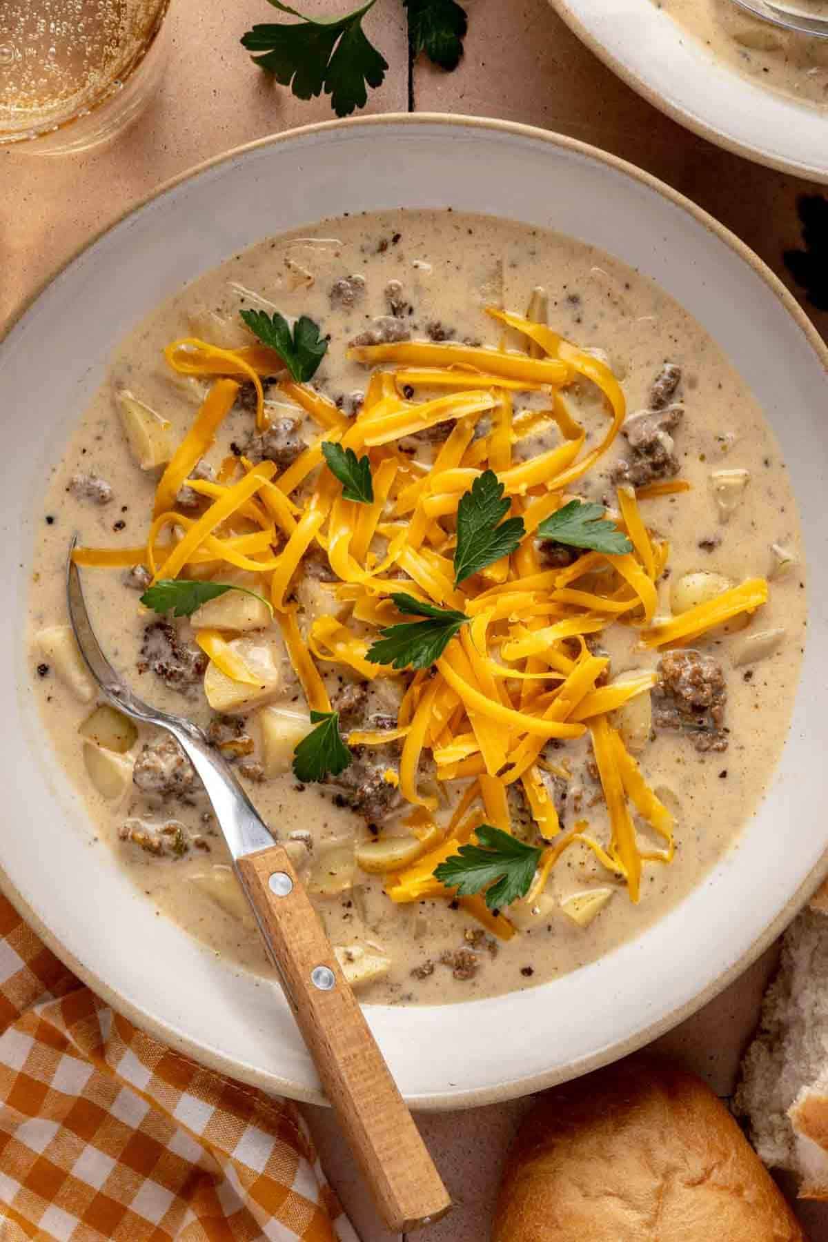 Cheeseburger soup topped with grated cheddar cheese in a white bowl with a spoon.