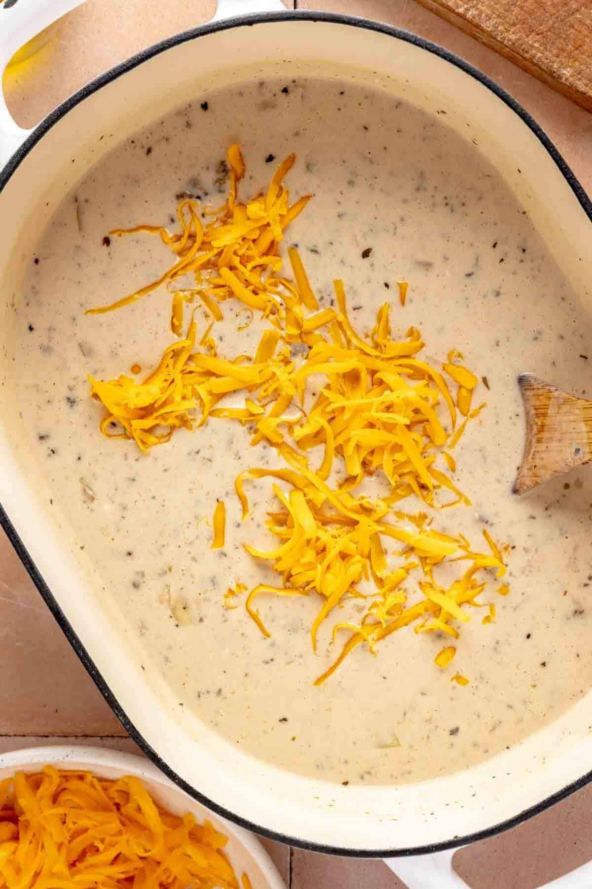 Using a wooden spoon to stir grated cheese into soup.