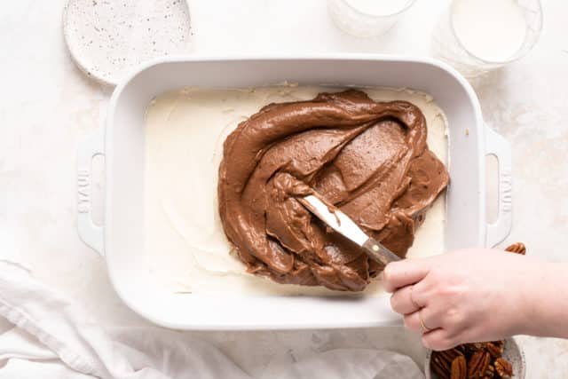 woman's hand spreading chocolate pudding layer over cream cheese layer