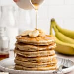 Drizzling maple syrup over a stack of banana pancakes.