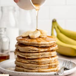 Drizzling maple syrup over a stack of banana pancakes.