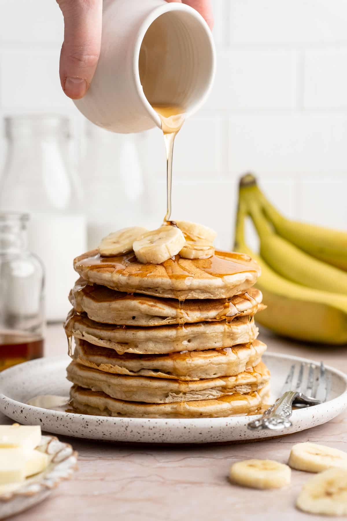 Drizzling maple syrup over a stack of banana pancakes.