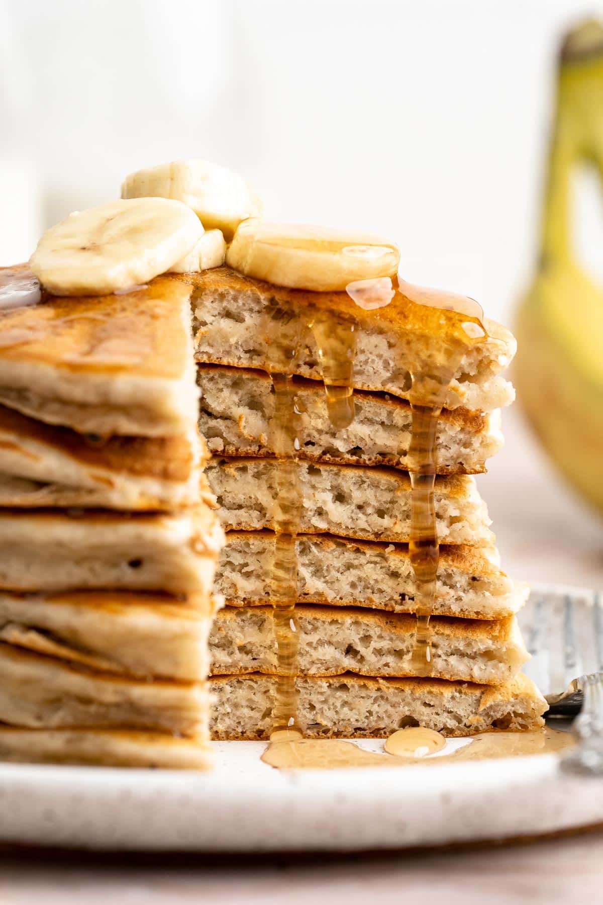 A stack of banana pancakes with a bite taken out and syrup drizzling down the side.