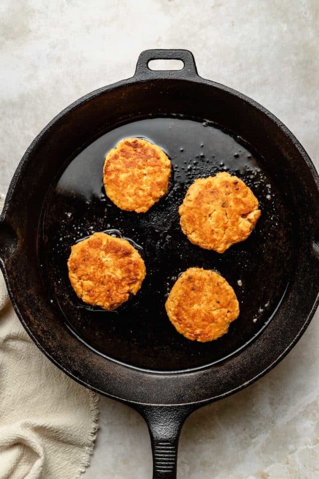 salmon patties cooking in an iron skillet