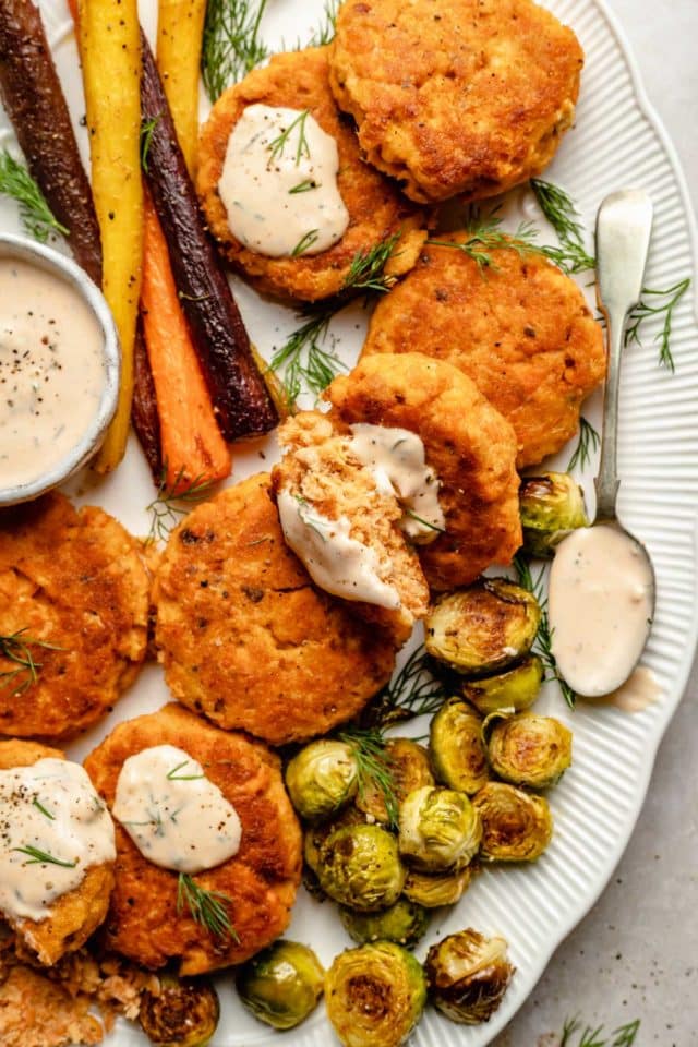 plate filled with salmon patties, small bowl of sauce and roasted vegetables