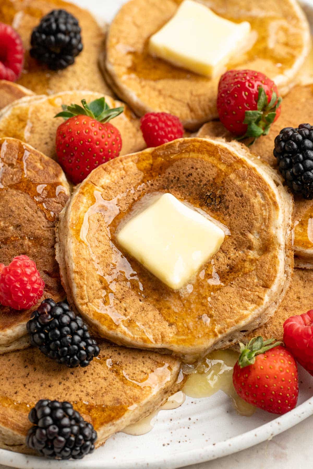 A plate of pancakes topped with pats of butter, syrup and berries.