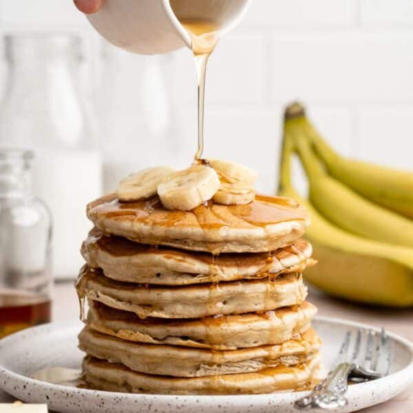 Drizzling maple syrup over a stack of banana pancakes.