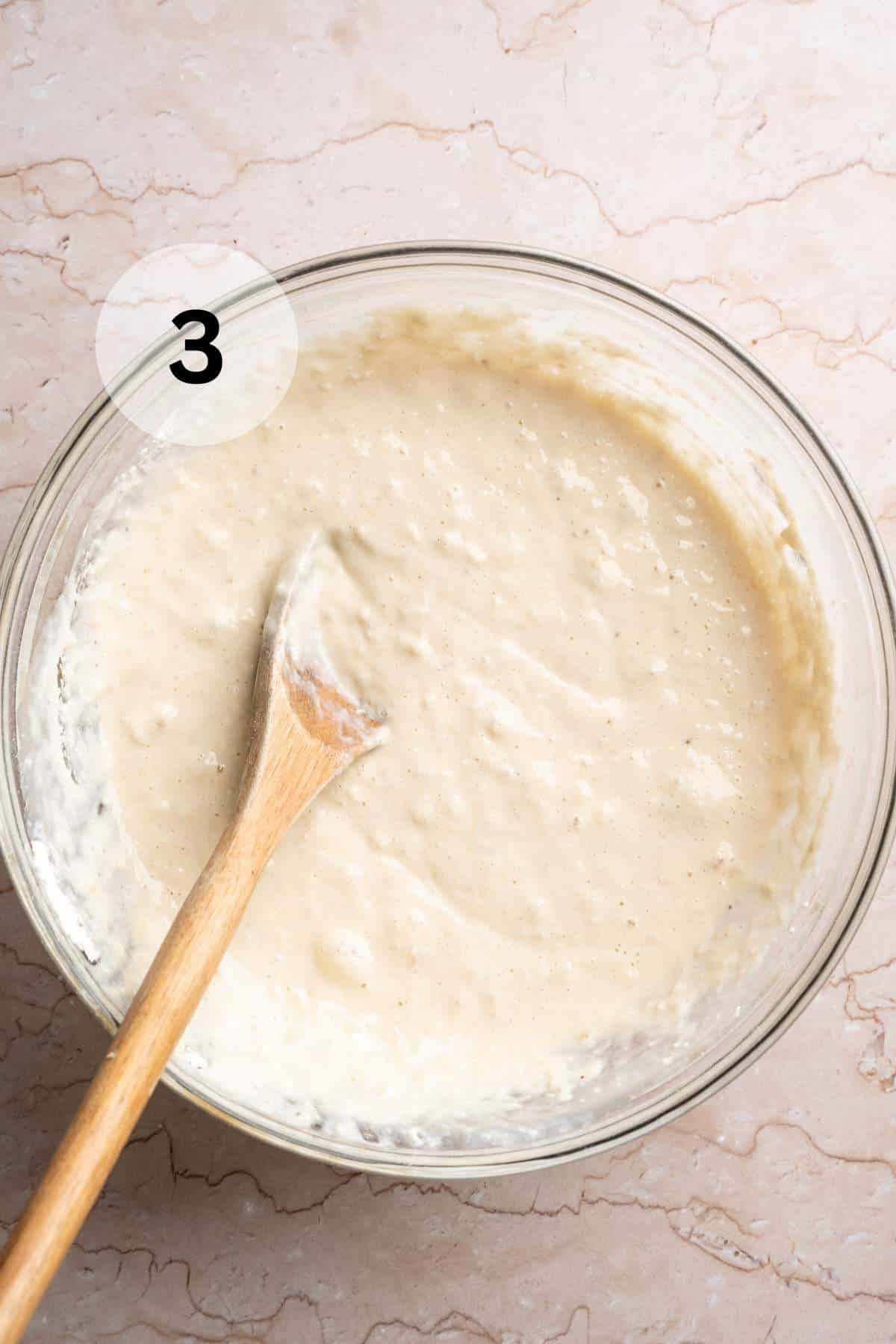 Using a wooden spoon to stir pancake batter in a large bowl.