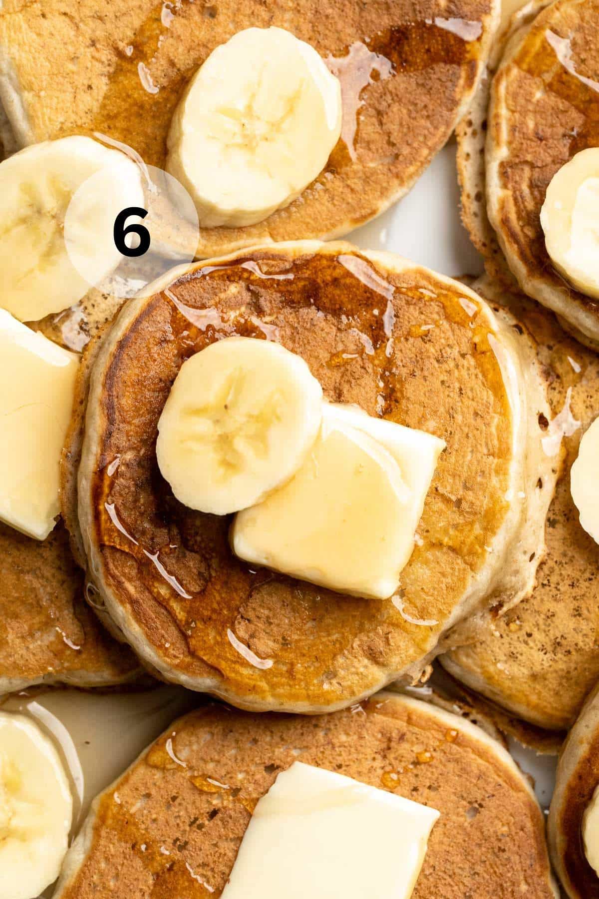 Pancakes on a plate topped with butter, banana slices and maple syrup.