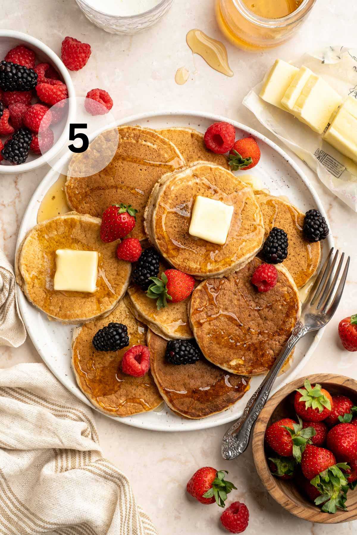 Whole wheat pancakes on a plate with butter and berries.