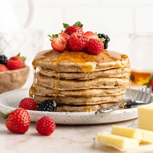 A stack of whole wheat pancakes topped with berries and syrup.