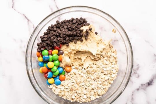 mixing oats, chocolate chips, and M&M's with cookie dough batter