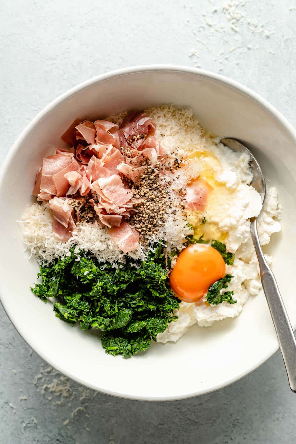 Stirring together spinach, egg, cheese and prosciutto.