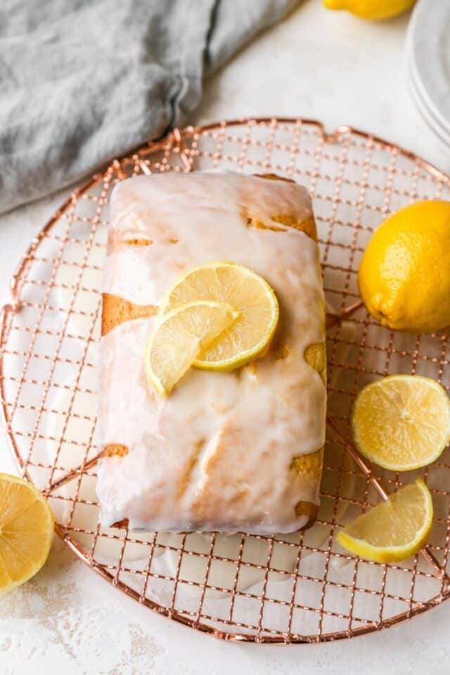 Loaf of bread on a wire rack topped with glaze and slices of lemon.