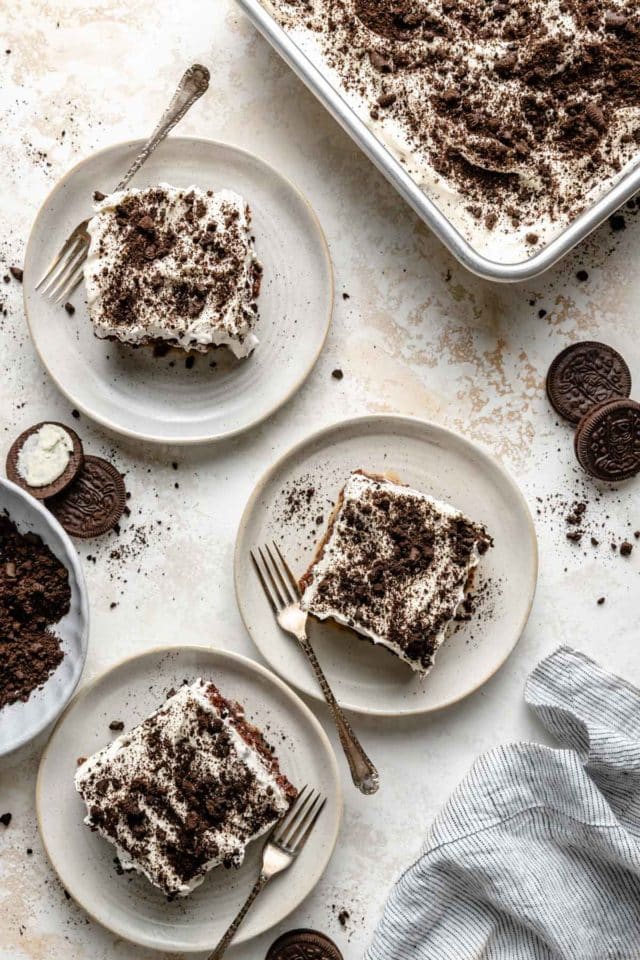 Slices of chocolate cake on plates with Cool Whip and Oreo crumbs.