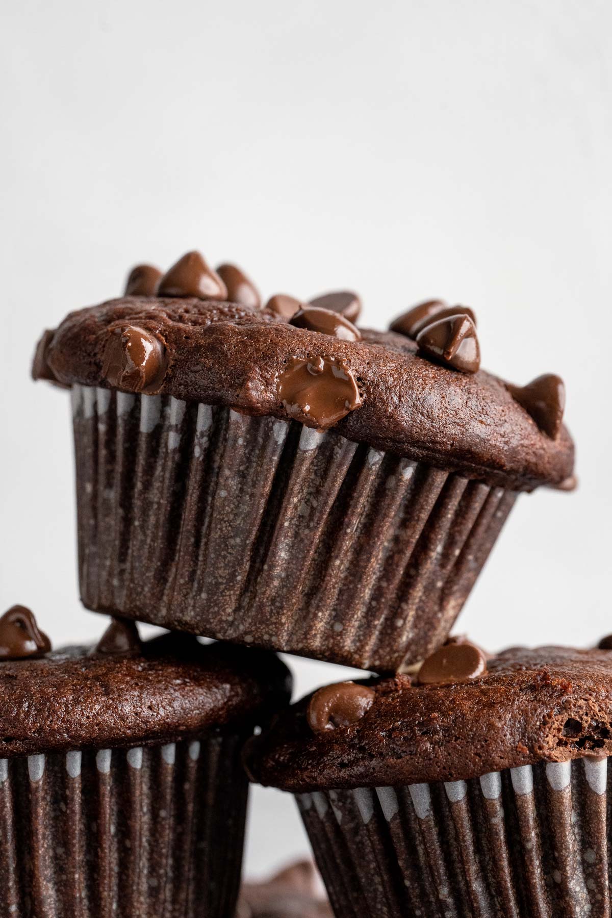 Chocolate chocolate chip banana muffin stacked on other chocolate muffins.