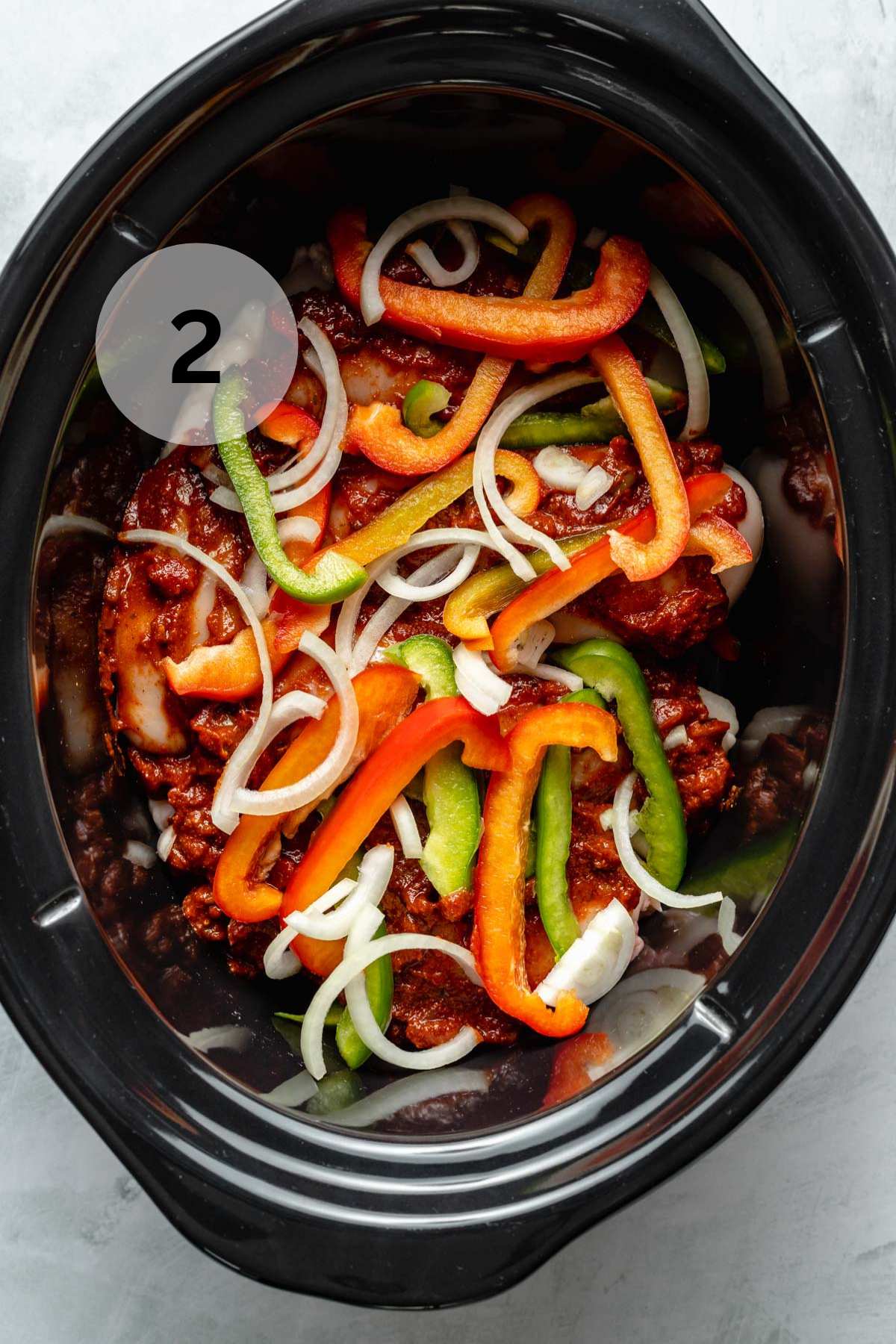 Adding chicken and sliced bell peppers and onions to a slow cooker.