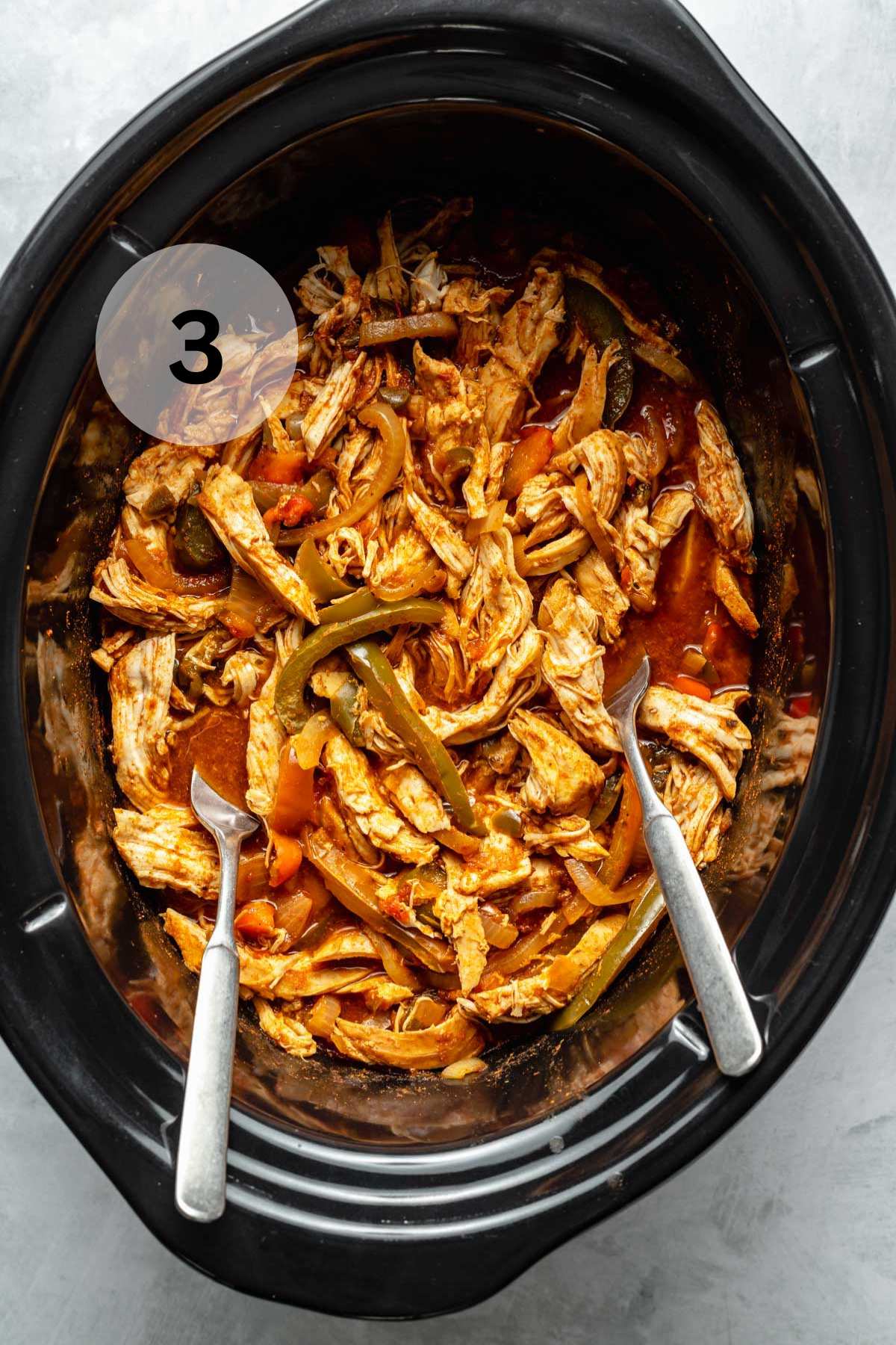 Shredded chicken in a slow cooker with 2 forks.