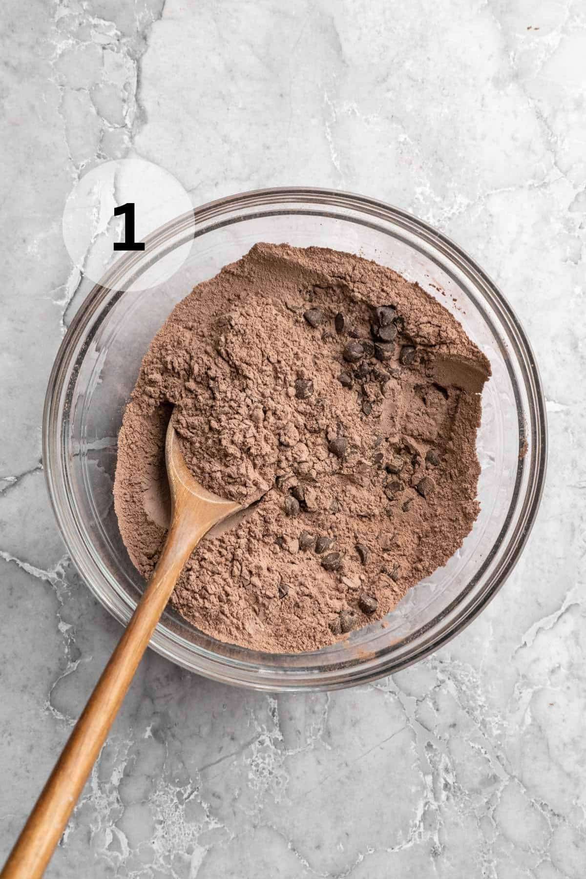 Using a wooden spoon to stir flour, cocoa powder and chocolate chips.