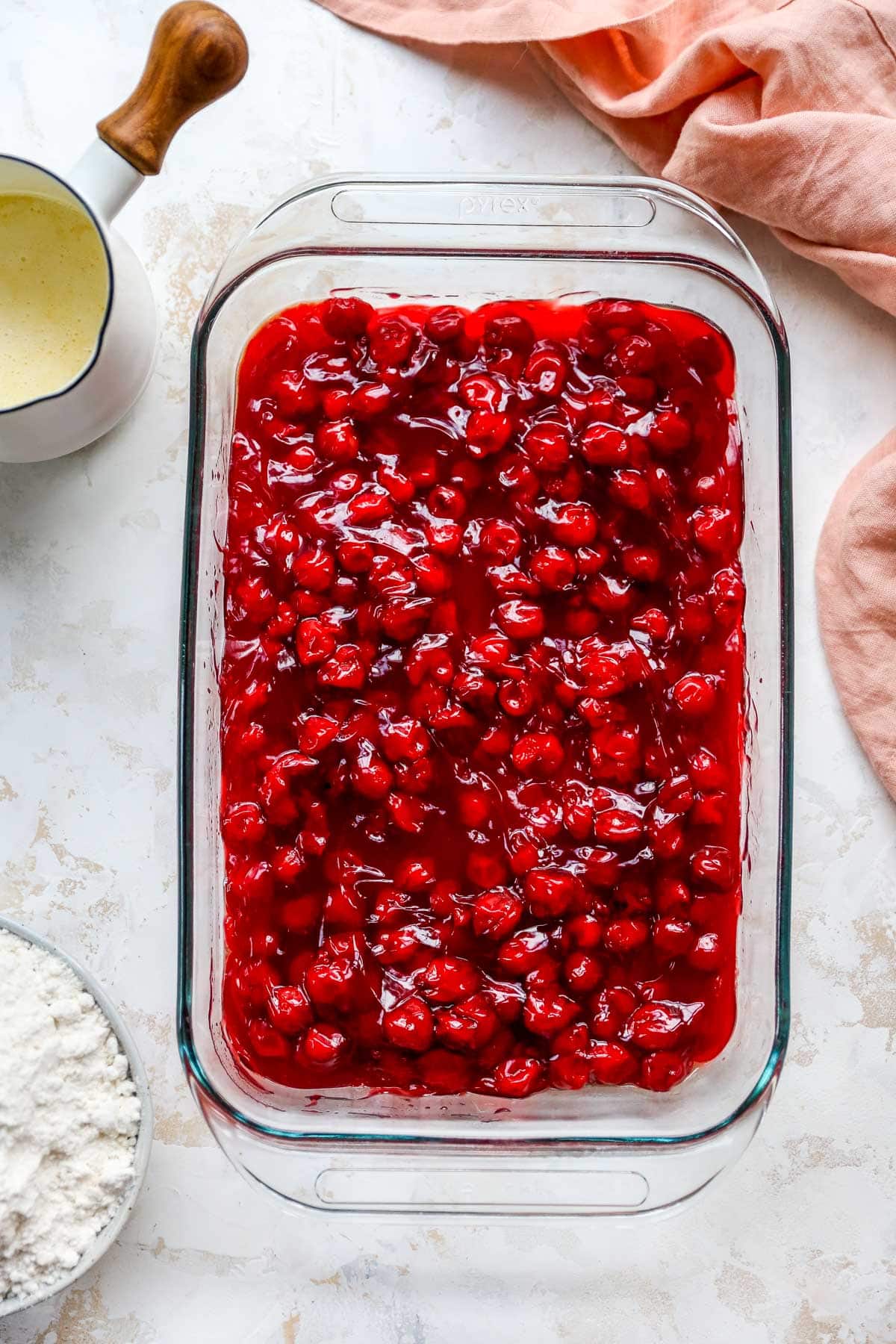 Adding cherry pie filling to a glass dish.
