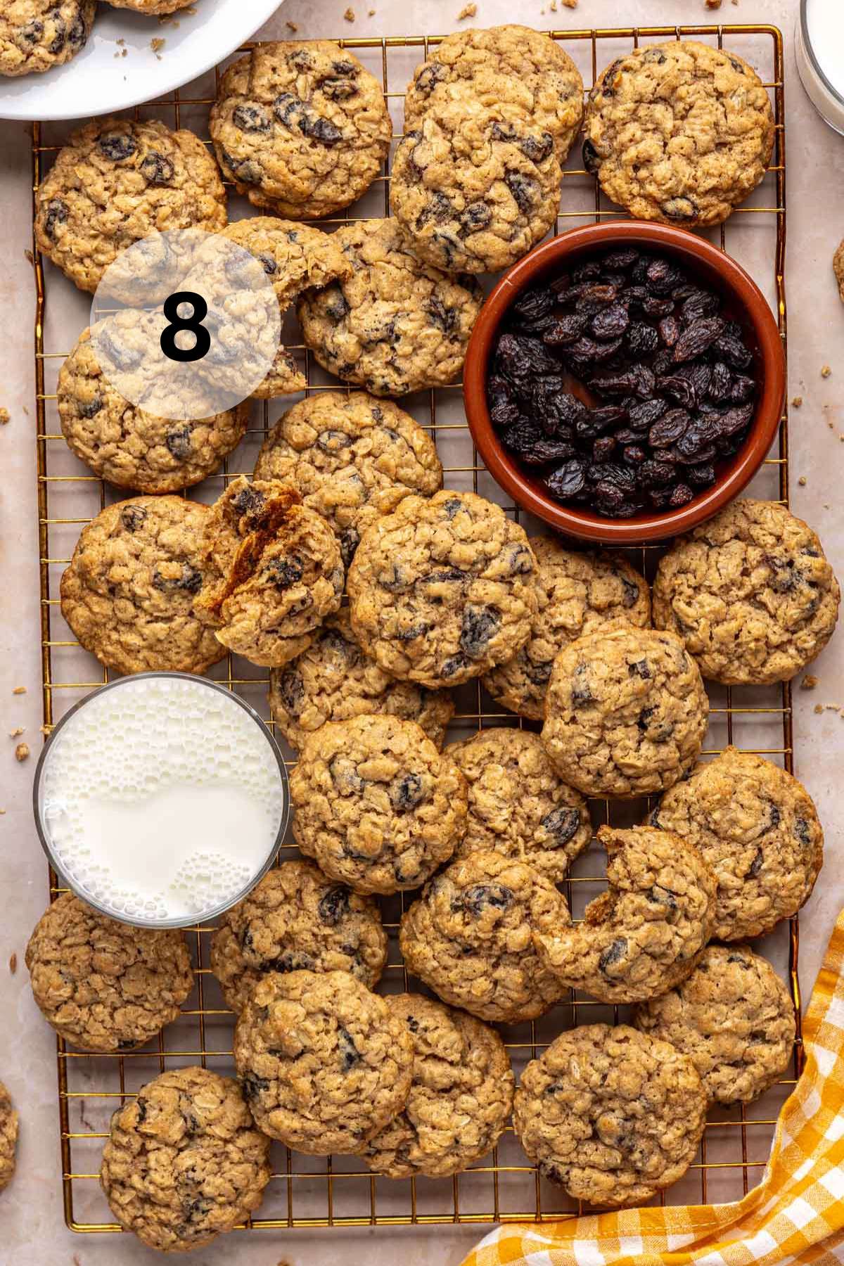 Oatmeal raisin cookies on a wire rack near a glass of milk and small bowl of raisins.