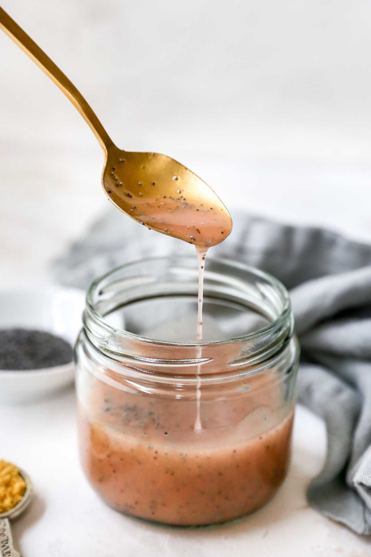 Drizzling dressing from a spoon into a glass jar.