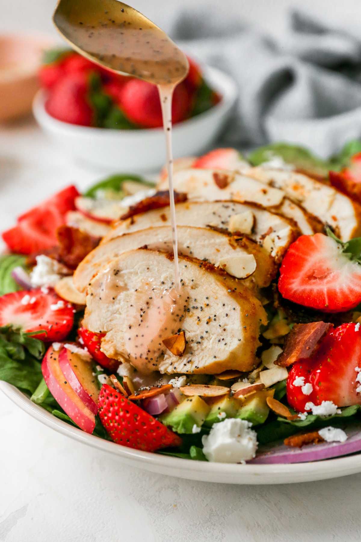 Drizzling poppy seed dressing over a strawberry salad.