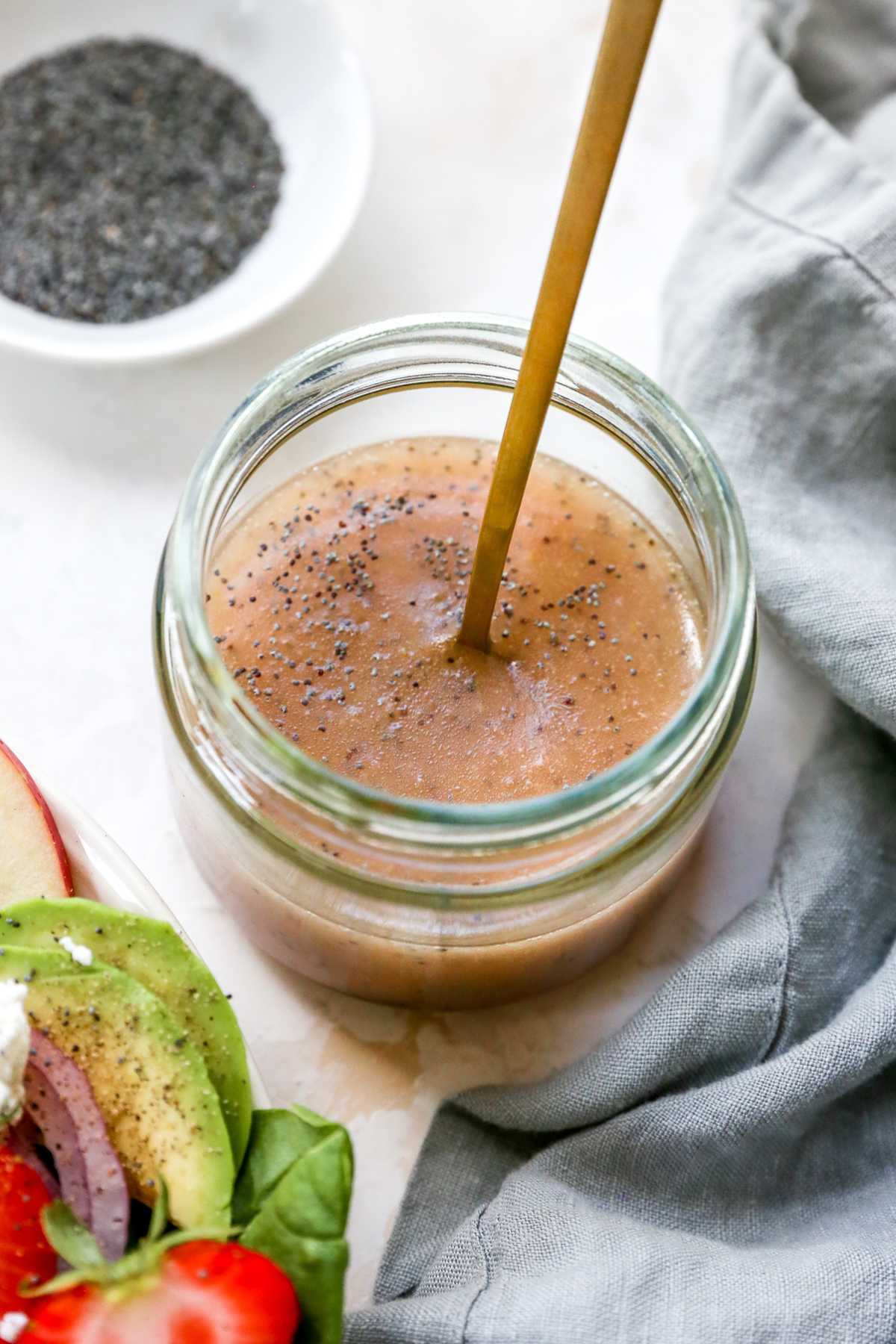 Poppy seed dressing in a jar near a small white bowl of poppy seeds.