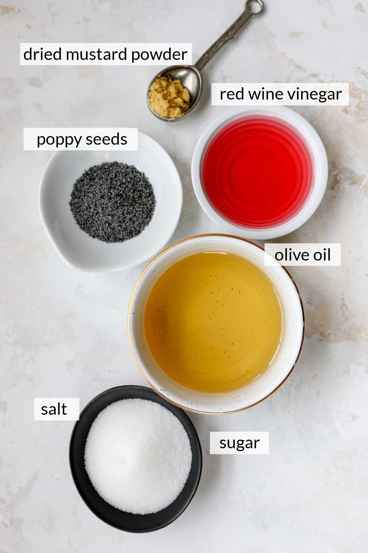 Red wine vinegar, olive oil, sugar, poppy seeds and mustard powder in small bowls.