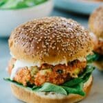 Salmon burger on a sesame seed bun with ranch and spinach.