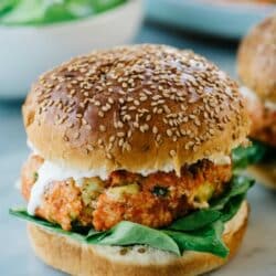 Salmon burger on a sesame seed bun with ranch and spinach.