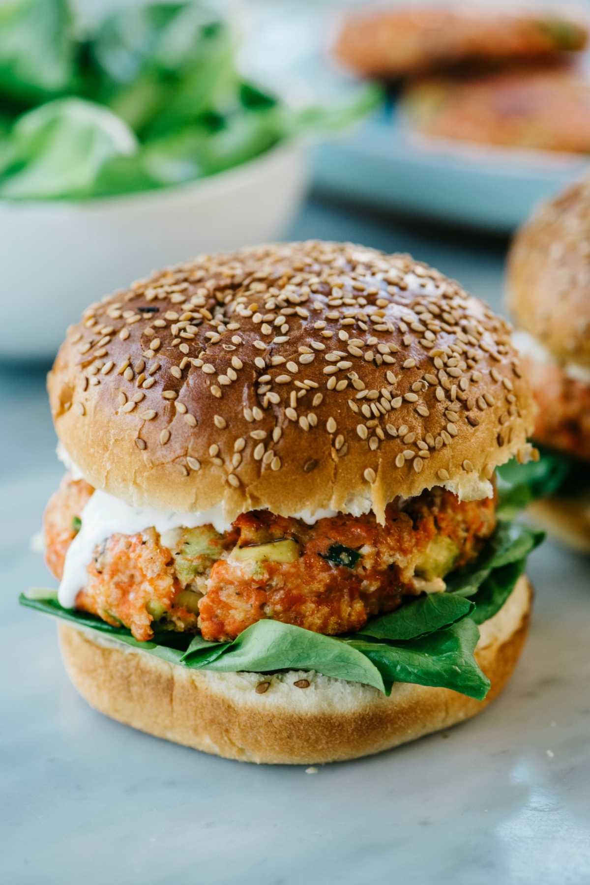 Salmon burger on a sesame seed bun with ranch and spinach.