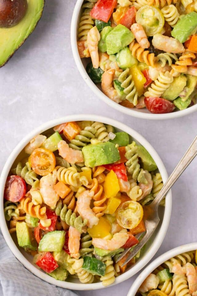 Colorful pasta salad with shrimp divided into small white bowls.