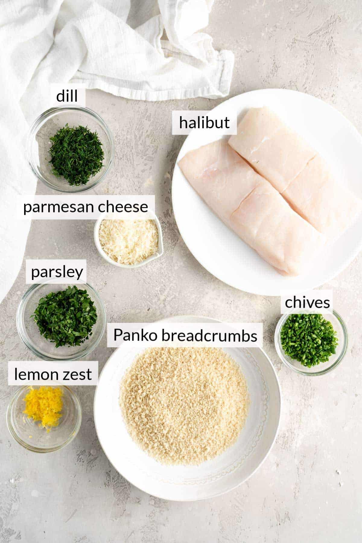 Two halibut filets on a plate near a bowl of breadcrumbs, lemon zest, parmesan cheese and fresh dill.