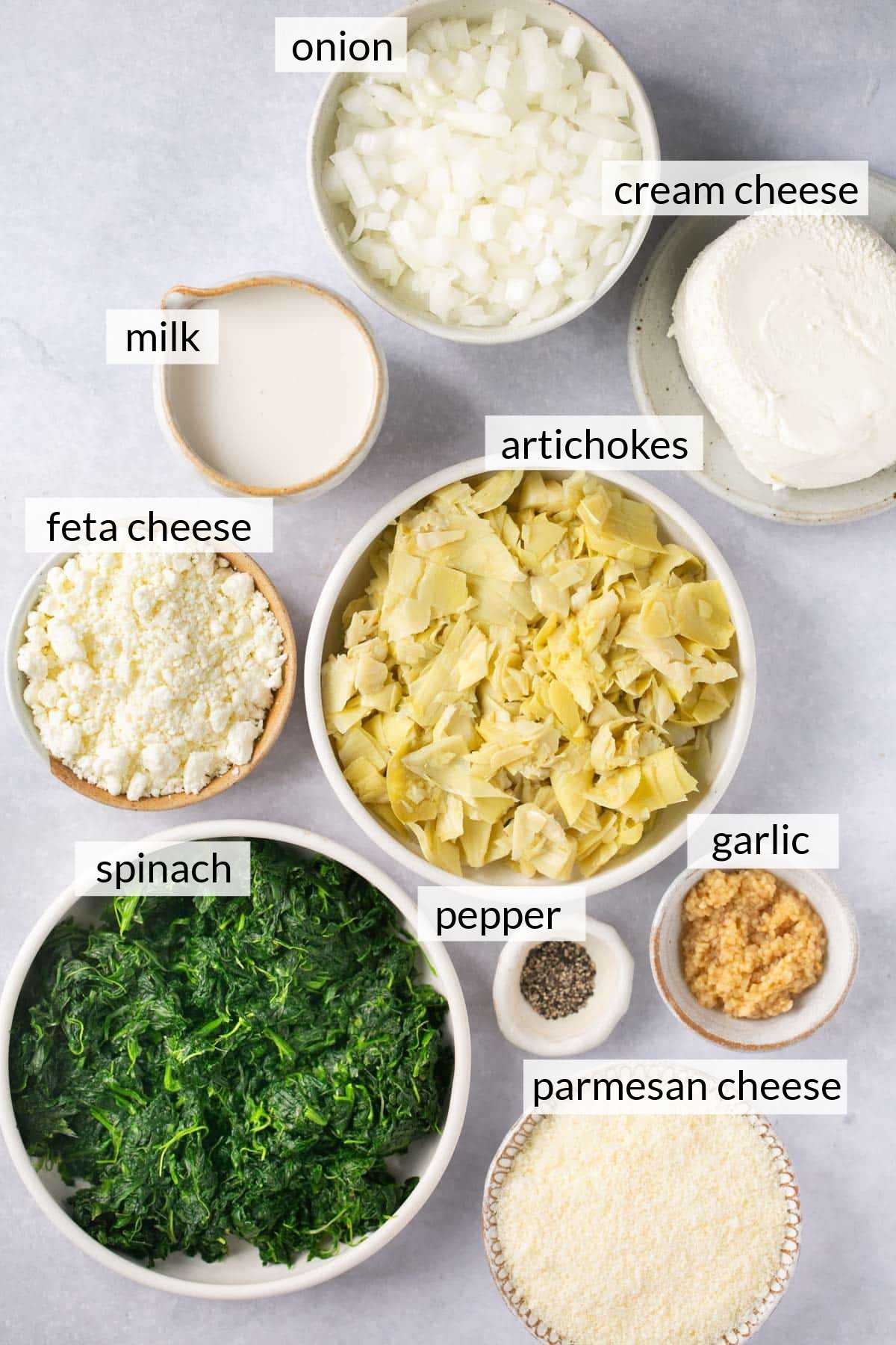 Spinach, artichokes, cream cheese, milk, parmesan cheese and feta cheese divided into small bowls.