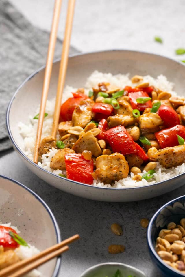 Chicken and veggies over rice served with chopsticks.