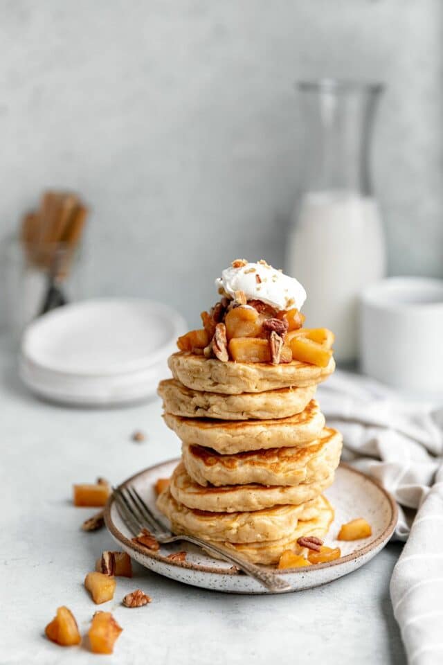 A stack of apple pancakes topped with diced apples and whipped cream.